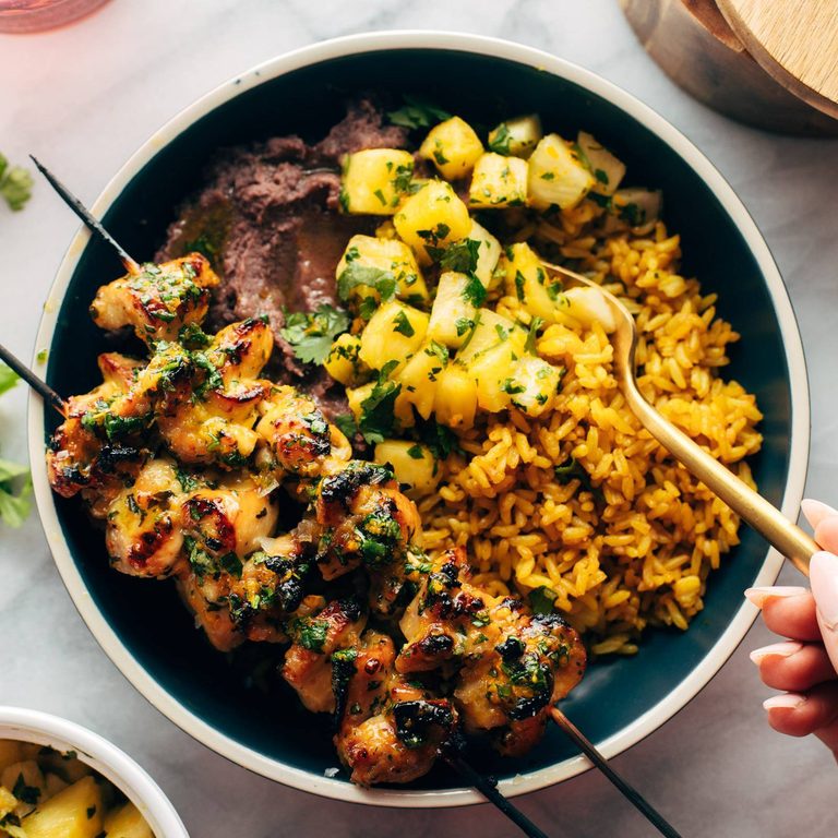 Cilantro orange chicken in a bowl with rice, pineapple, and beans.