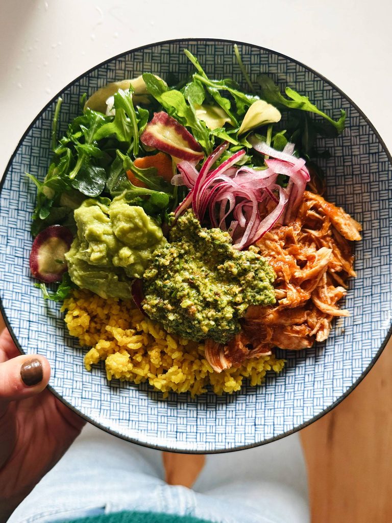 Crockpot chicken in a bowl with rice and greens.